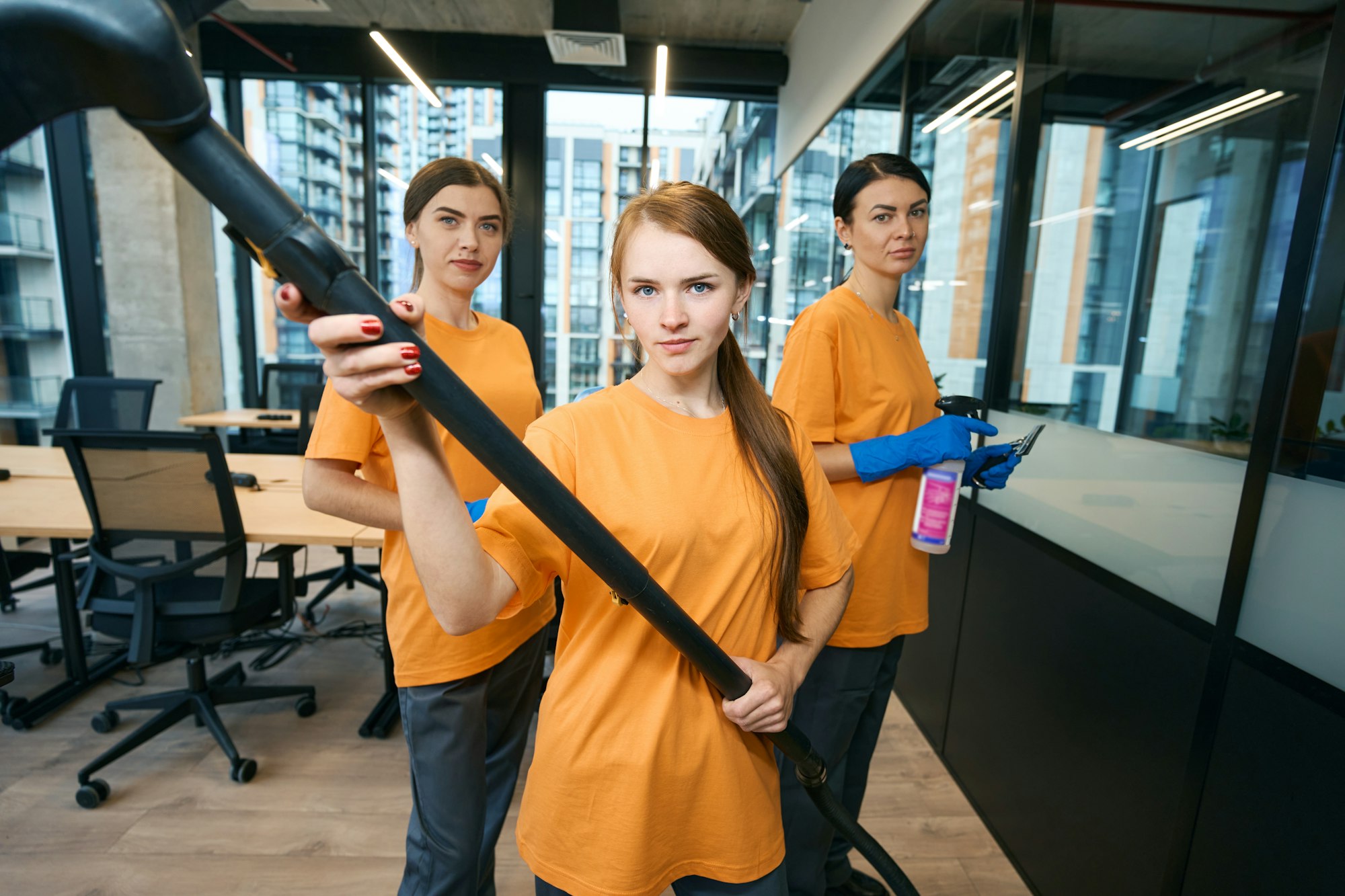 Three cleaning company workers in uniform cleaning and disinfecting office space